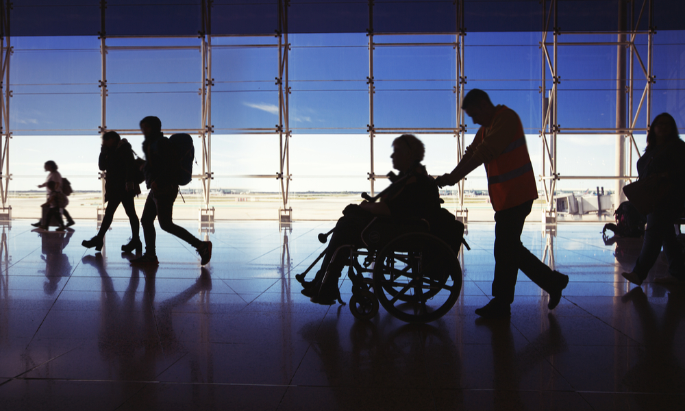 Silhouette of man in wheelchair and people carrying luggage and walking in airport