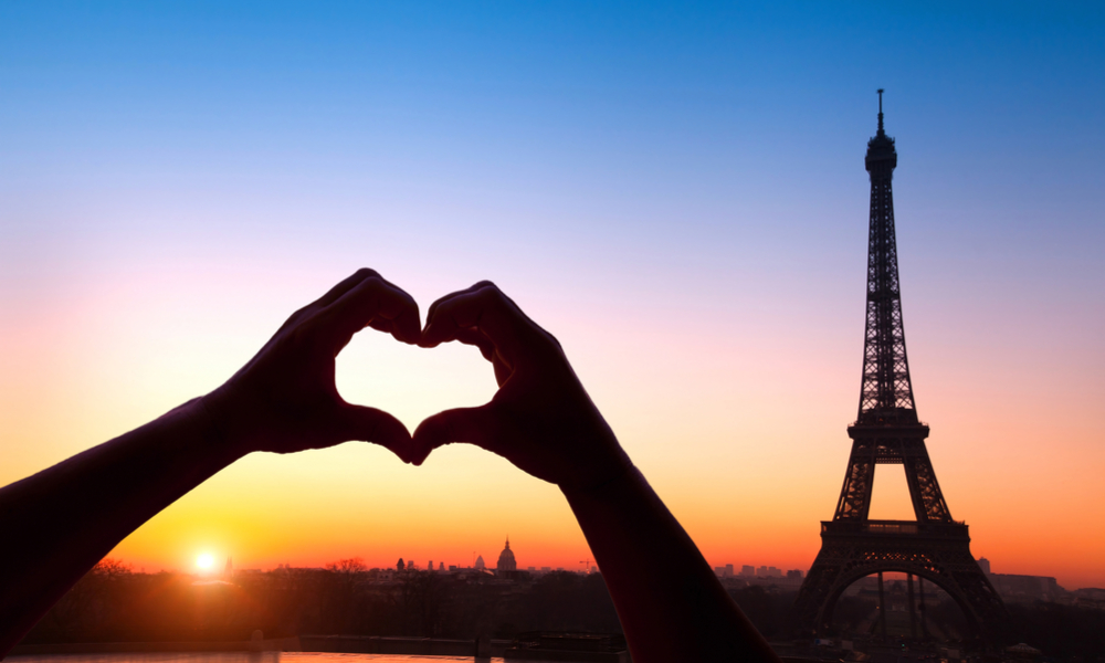 a person making heart shape with hands, eiffel tower in background, Paris