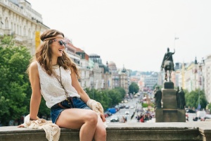 Happy young woman tourist in boho chic clothes relaxing on parapet in the historical center of Prague