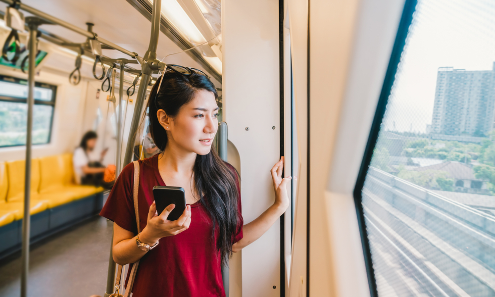 how to stay safe abroad: woman passenger with casual suit using smart mobile phone in the Skytrain rails or subway for travel in the big city
