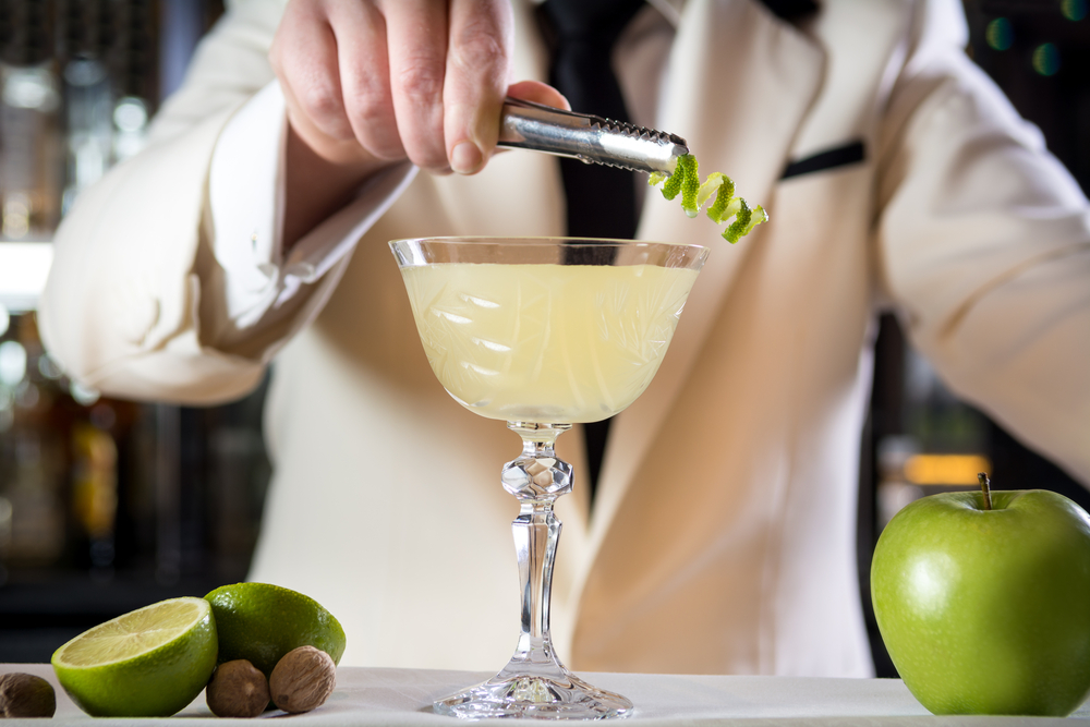 Classy bartender barman decorating rum based drink cocktail lime zest shaker in bar uniform cruise ship