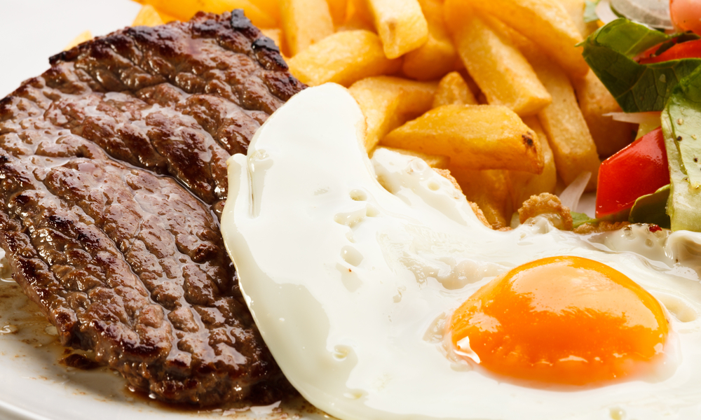 Grilled steaks, French fries, fried egg and vegetables