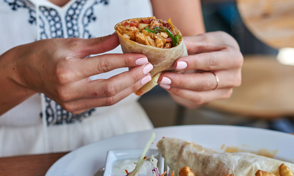 Female hands holding tasty mexican burrito with different ingredients inside.
